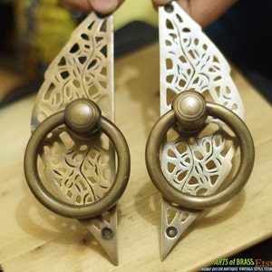 May include: Two ornate brass door pulls with a leaf design and a ring handle. The pulls are in a vintage style and have a distressed finish.