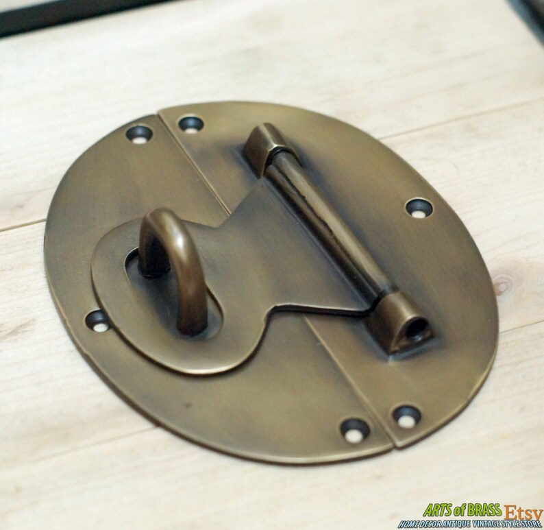 May include: A brass oval-shaped latch with a hasp and a sliding bolt. The latch has a smooth, polished finish and is designed for use on a wooden chest or box.