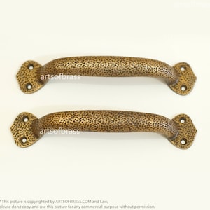 Peut inclure: Deux poignées de porte en laiton antique avec une finition martelée. Les poignées mesurent environ 15 cm de long et ont une extrémité en forme de diamant.