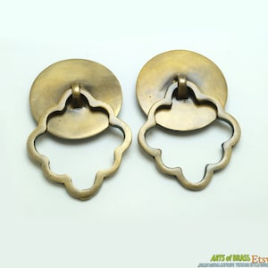 Può includere: Due tiretti per porte di armadio in ottone antico con un design floreale decorativo. I tiretti hanno una base rotonda e una maniglia ad anello.