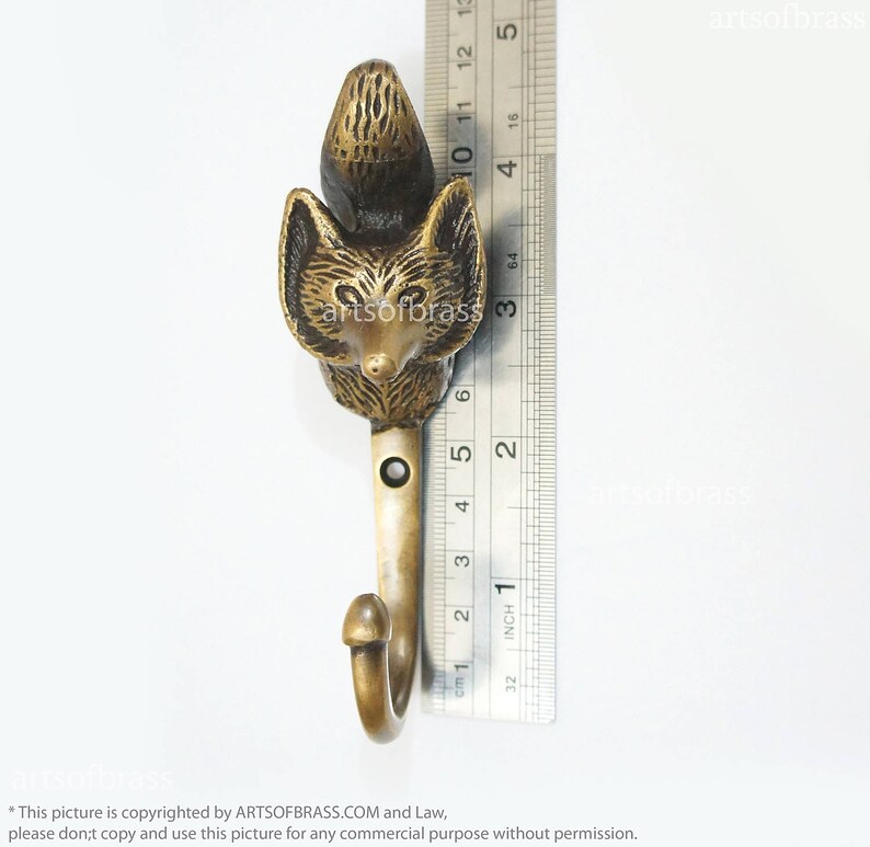 May include: A brass fox hook with a detailed design. The hook is about 3 inches long and has a rounded top. The fox's face is facing forward with a black nose and eyes.