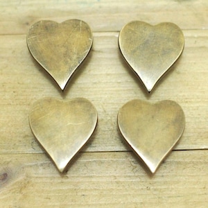May include: Four brass heart-shaped drawer pulls. The pulls are smooth and have a slightly aged finish.