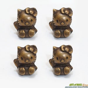 May include: Four brass-colored Hello Kitty figurines. Each figurine is about 1 inch tall and features a sitting Hello Kitty with a bow on her head.