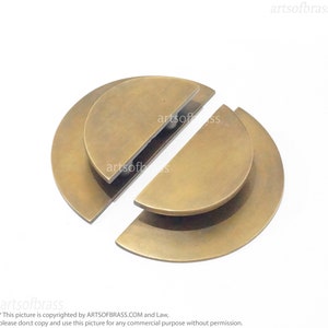 May include: Two brass half-circle door pulls, each with a slightly raised edge, are shown on a white background. The pulls are separated, with the top half of the pull on the left and the bottom half of the pull on the right.