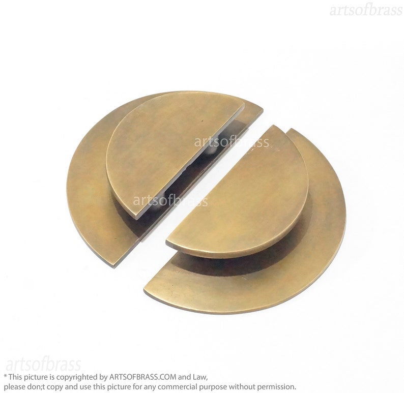 May include: Two brass half-circle door pulls, each with a slightly raised edge, are shown on a white background. The pulls are separated, with the top half of the pull on the left and the bottom half of the pull on the right.
