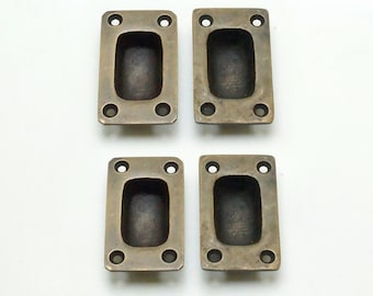 May include: Four antique brass cabinet pulls with a rectangular shape and a recessed center. The pulls have four small holes for mounting.