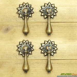 May include: Four antique brass cabinet pulls with ornate floral designs. Each pull has a teardrop-shaped handle and a decorative rosette.
