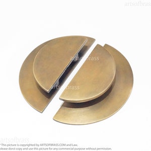 May include: Two brass half-circle door pulls, one on top of the other, with a slightly rounded edge. The pulls are separated and ready to be installed.