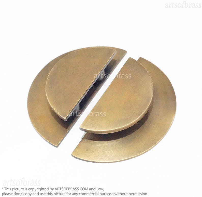 May include: Two brass half-circle door pulls, one on top of the other, with a slightly rounded edge. The pulls are separated and ready to be installed.