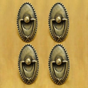 Peut inclure: Quatre poignées de porte de placard ovales en laiton antique avec une poignée en anneau. Chaque poignée a un motif décoratif autour du bord et un centre surélevé.