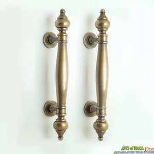 May include: Two antique brass door handles with a traditional design. The handles are long and have a rounded, bulbous shape at the top and bottom.