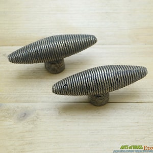May include: Two antique brass cabinet knobs with a textured, ribbed design. The knobs have a dark, aged finish and are mounted on small, round bases. These decorative knobs are ideal for adding a vintage touch to furniture.
