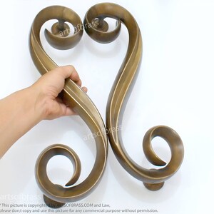 May include: A pair of ornate, gold-toned, metal door handles in the shape of a heart. The handles are intricately designed with swirling patterns and have a smooth, polished finish.