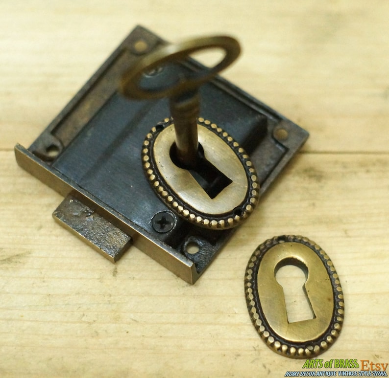 May include: Antique brass keyhole escutcheon with a key in the keyhole. The escutcheon has a decorative beaded border.