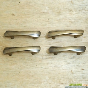 May include: Four antique brass cabinet drawer pulls with a twisted design. The pulls are approximately 6.5 cm long.