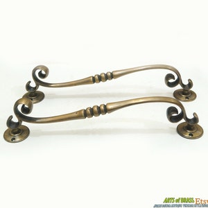 以下が含まれることがあります： 装飾的なスクロールデザインとビーズ状の中央部分を持つ、アンティークブラス製のドアハンドル2個。ハンドルの長さは約25cmです。