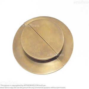 May include: A brass door pull with a circular design. The pull is made of two overlapping pieces, each with a semi-circular shape.