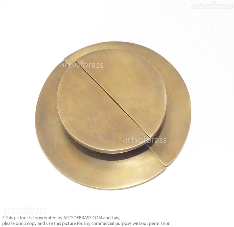 May include: A brass door pull with a circular design. The pull is made of two overlapping pieces, each with a semi-circular shape.