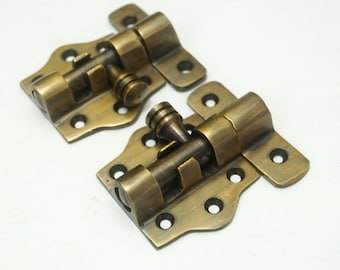 May include: Two antique brass door bolt latches with a decorative design. The latches have a round knob and a rectangular plate with multiple holes.
