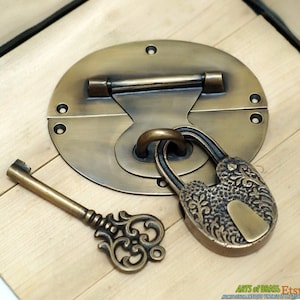 May include: Brass oval lock with a keyhole and a decorative padlock with a key. The lock is attached to a wooden surface.