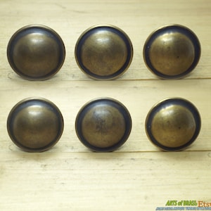 May include: Six antique brass cabinet knobs with a domed top and a raised rim. The knobs have a slightly aged, worn look.