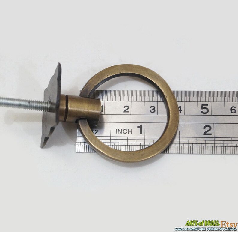 Puede incluir: Tirador de anillo de lat&oacute;n para armario con placa de fijaci&oacute;n de tornillo. El anillo tiene un di&aacute;metro de 2,5 cm. El herraje se mide con una regla.