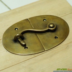 May include: A brass oval-shaped latch with a curved handle and a round knob. The latch is made of solid brass and has a polished finish.