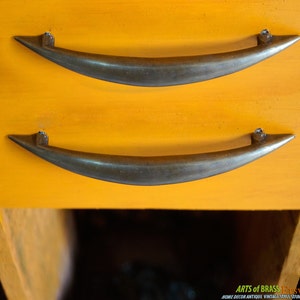 Puede incluir: Dos tiradores de cajón de metal vintage en forma de media luna, montados en una superficie naranja brillante.