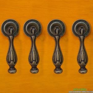 May include: Four antique brass cabinet pulls with a decorative design. The pulls have a round top and a teardrop-shaped body.