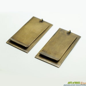 May include: Two brass rectangular tags with a slightly raised edge. The tags are layered on top of each other, creating a unique design.