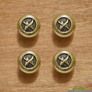 Può includere: Quattro pomelli rotondi dorati per armadio con un centro marrone scuro e un design decorativo di una farfalla stilizzata con spade incrociate.