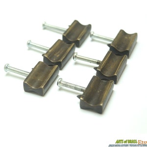 May include: Six antique brass cabinet knobs with a curved design and silver screws. The knobs are arranged in a staggered pattern on a white surface.