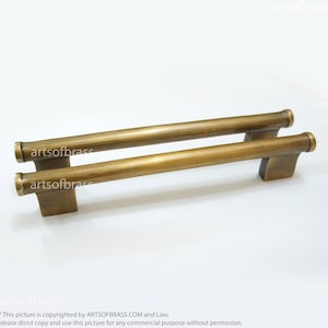 May include: A pair of antique brass cabinet pulls with a simple, rectangular design. The pulls are made of solid brass and have a brushed finish.