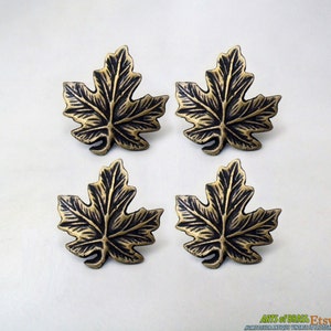 May include: Four antique brass maple leaf drawer pulls. The leaves are detailed with a black finish and have a slightly raised texture.