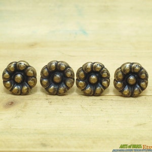 Może przedstawiać: Cztery antyczne mosiężne gałki do szafek z kwiatowym wzorem. Każda gałka ma wypukły centralny okrąg otoczony pierścieniem mniejszych okręgów.