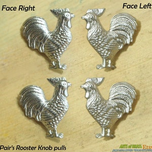 Puede incluir: Par de tiradores de pomo de puerta de gallo plateado. Los gallos están mirando en direcciones opuestas. El texto "Pair's Rooster Knob pulls" está en la parte inferior de la imagen.