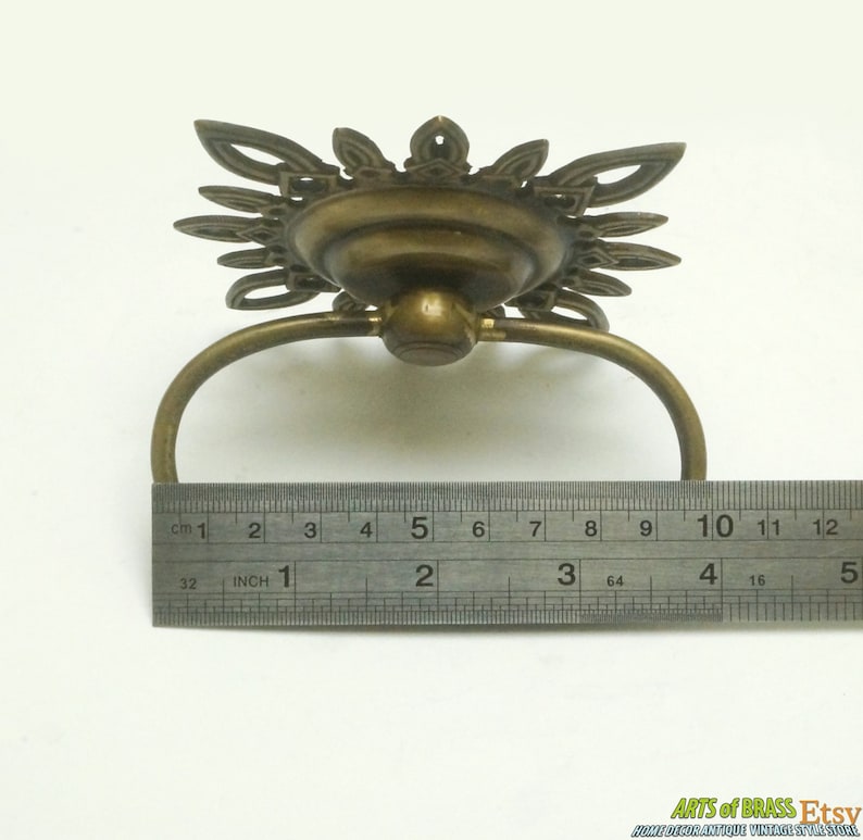 May include: A brass drawer pull with a decorative, ornate design. The pull is 2 inches wide and has a ring handle.
