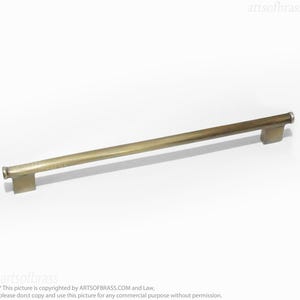 Puede incluir: Un tirador de armario largo, recto, de metal de color dorado con extremos redondeados. El tirador mide aproximadamente 30 cm de largo.