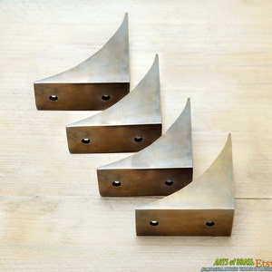 Puede incluir: Cuatro soportes de esquina de latón con un diseño curvo. Cada soporte tiene tres agujeros para montaje.