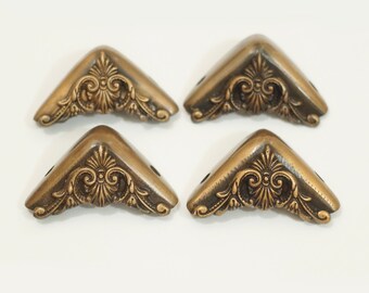 May include: Four antique brass corner protectors with ornate floral designs. Each corner protector has two screw holes.