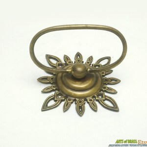 May include: A brass towel ring with a decorative sunburst design. The ring is oval shaped and has a smooth, polished finish.
