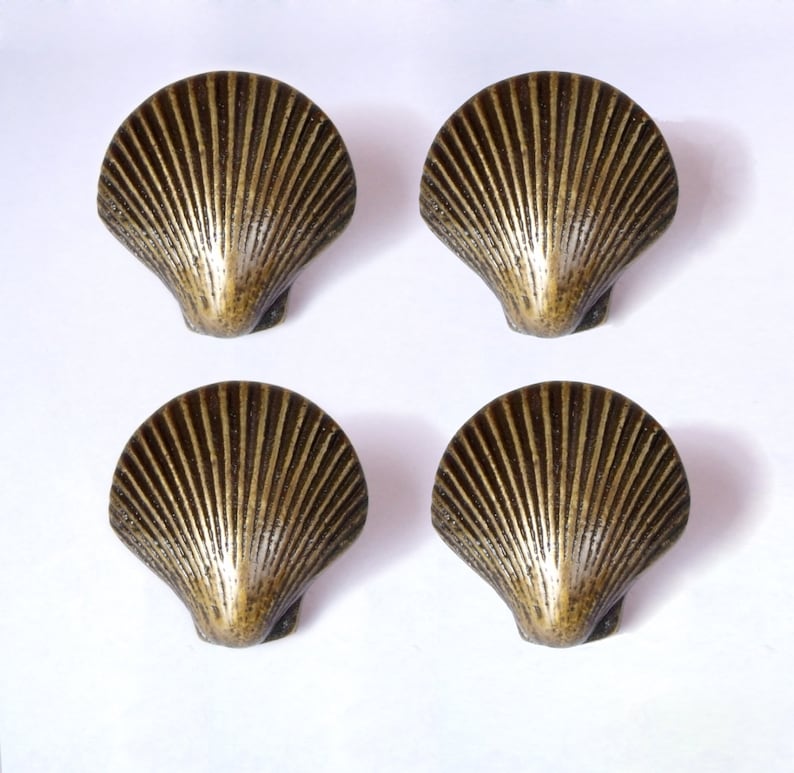 May include: Four antique gold-toned seashell-shaped cabinet knobs. Each knob features a detailed, raised design of a seashell with a textured surface.