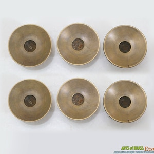 May include: Six antique brass candle holders with a circular base and a central hole for a candle. The holders have a worn, aged finish.