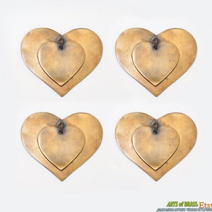 Puede incluir: Cuatro colgantes en forma de corazón de latón, cada uno con un corazón más pequeño en su interior. Los corazones son de color dorado cálido y tienen un aspecto ligeramente envejecido.