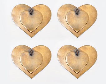 Puede incluir: Cuatro colgantes en forma de corazón de latón, cada uno con un corazón más pequeño en su interior. Los corazones son de color dorado cálido y tienen un aspecto ligeramente envejecido.
