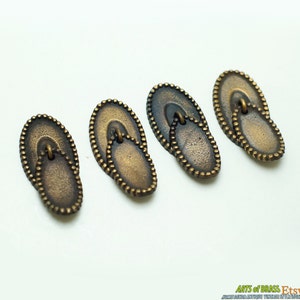 Peut inclure: Quatre tirettes de tiroir ovales en laiton antique avec un bord perlé décoratif. Chaque tirette a une poignée en boucle.