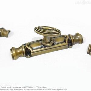 May include: A brass window latch with an oval-shaped handle. The latch has a decorative design and is in a vintage style.