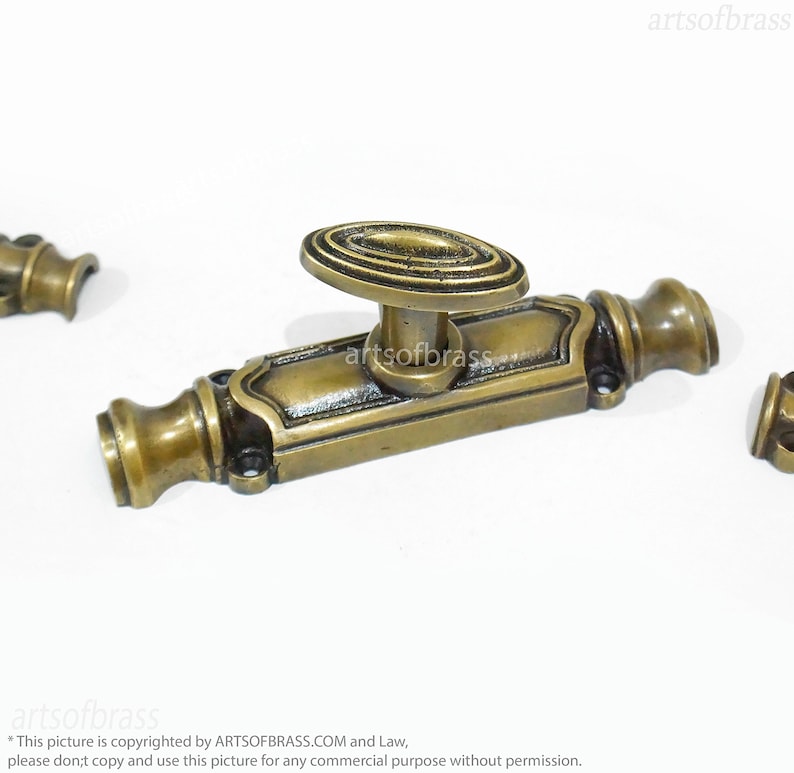 May include: A brass window latch with an oval-shaped handle. The latch has a decorative design and is in a vintage style.