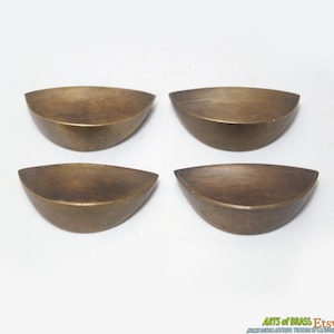 Może przedstawiać: Zestaw czterech antycznych mosiężnych gałek do szafek, każda w kształcie półkola z gładką, lekko zaokrągloną powierzchnią.