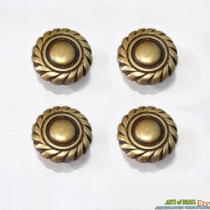 May include: Four antique brass cabinet knobs with a rope design around the edge and a raised center. The knobs are approximately 1 inch in diameter.